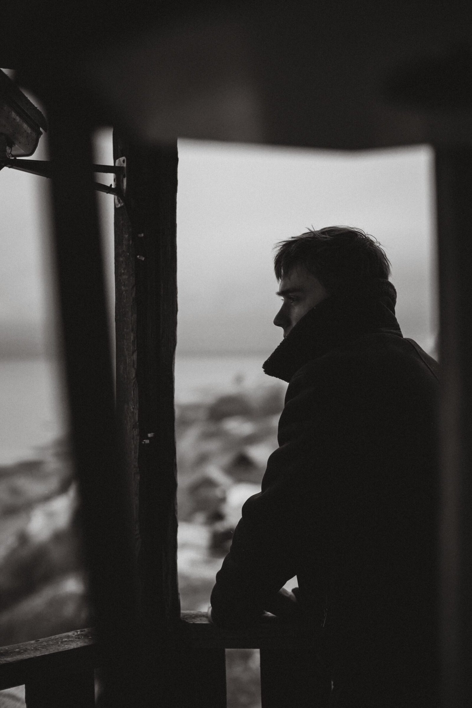 Silhouette of a man in a coat gazing at a bleak landscape, captured in black and white.